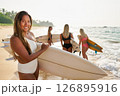 Group of young women with surfboards walk on sunny tropical beach. Surfers wear swimwear and prepare for ocean surfing. Friends enjoy water sport, adventure and travel at seaside holiday. 126895916