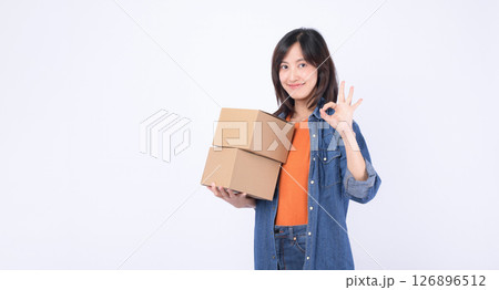 Southeast asian woman holding cardboard boxes shows ok gesture while enjoying internet online shopping experience with cheerful smile on white background Southeast asian woman holding cardboard boxes shows ok gesture while enjoying internet online shopping experience with cheerful smile on white background 126896512