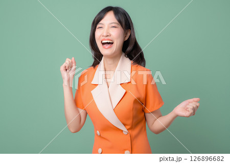 Southeast Asian woman in orange dress smiling and celebrating with joyful expression against green background, happiness and positive emotion concept Southeast Asian woman in orange dress smiling and celebrating with joyful expression against green background, happiness and positive emotion concept 126896682