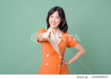 Southeast Asian woman smiling confidently in orange blazer points forward against green background showing positive and friendly expression Southeast Asian woman smiling confidently in orange blazer points forward against green background showing positive and friendly expression 126896687