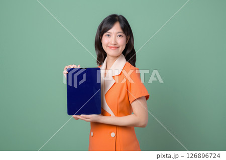 Southeast asian woman in orange suit holding blank blue tablet with cheerful expression on green background Southeast asian woman in orange suit holding blank blue tablet with cheerful expression on green background 126896724