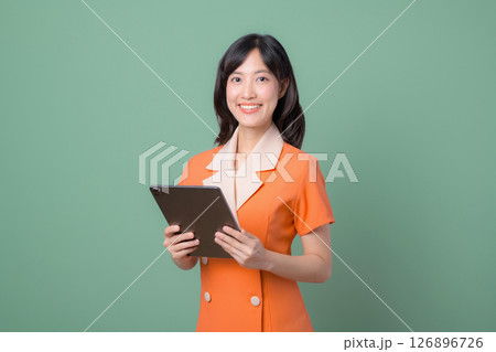 Southeast asian woman in orange dress holding tablet smiling confidently against green background modern professional portrait 126896726
