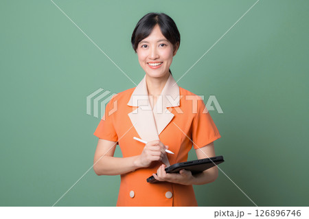 Southeast asian woman in orange dress holding digital tablet and stylus smiling confidently against green background Southeast asian woman in orange dress holding digital tablet and stylus smiling confidently against green background 126896746