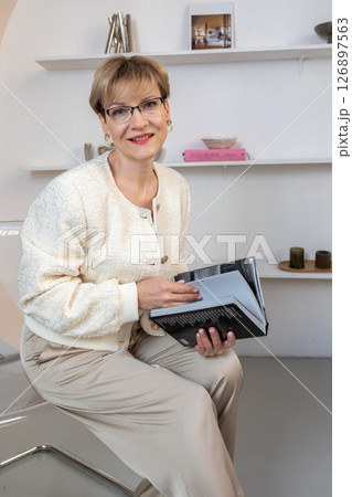 Portrait of smiling woman with glasses and book in her hands in bright room. Vertical photo. High quality photo 126897563