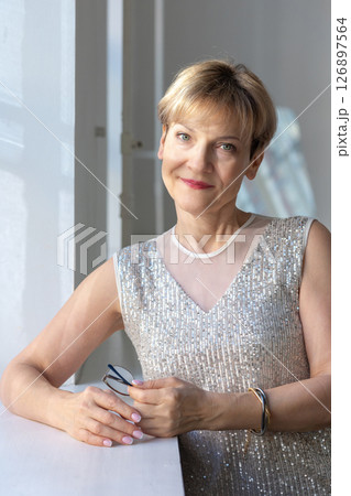 Portrait of smiling woman in festive clothes against a gray wall in a bright sunny room. Vertical photo. High quality photo 126897564