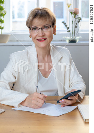 Portrait of business woman. Confident mature woman using mobile phone and typing. Vertical photo. High quality photo 126897621