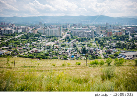 Scenic view of krasnoyarsk, russia, showcasing residential houses, apartment buildings, and mountains under a cloudy sky Scenic view of krasnoyarsk, russia, showcasing residential houses, apartment buildings, and mountains under a cloudy sky 126898032