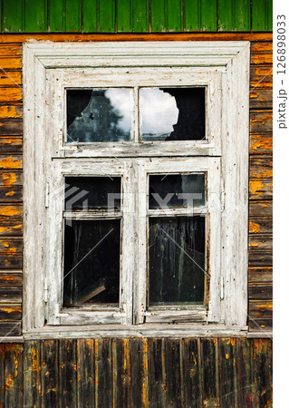 Broken window in old abandoned wooden house reflecting cloudy sky 126898033