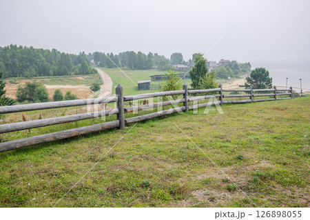 Scenic view of russian countryside with wooden fence, dirt road, forest, village and river in foggy morning 126898055