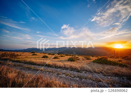 Sunset illuminating Crimean mountains and steppe landscape with dirt road Sunset illuminating Crimean mountains and steppe landscape with dirt road 126898062