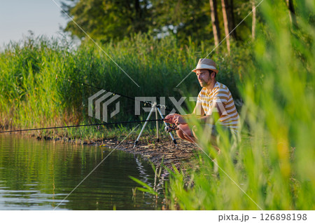 Man fishing by a lake during sunset. Man fishing by a lake during sunset. 126898198