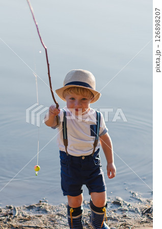 A small toddler boy standing by a lake at sunset. Copy space. A small toddler boy standing by a lake at sunset. Copy space. 126898207