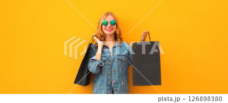 Shopping day, stylish beautiful happy smiling young woman with black shopping bags on yellow wall 126898380