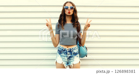 Stylish modern young woman posing wearing shorts, sunglasses on white wall background 126898381