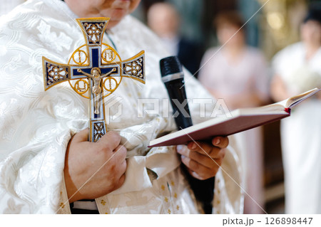 Priest Holding Cross and Reading from Holy Book during Ceremony Priest Holding Cross and Reading from Holy Book during Ceremony 126898447