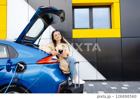 Young woman waiting charging automobile battery from small public station and using smartphone while charging automobile 126898560