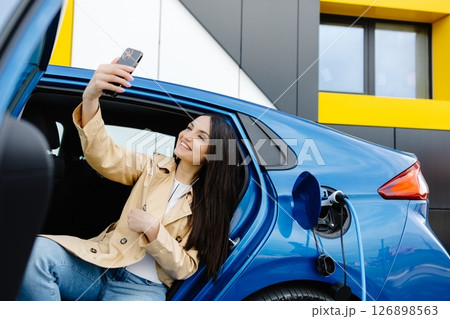 Business lady sitting inside charging electric car and using modern smartphone. Technology and transport concept. 126898563