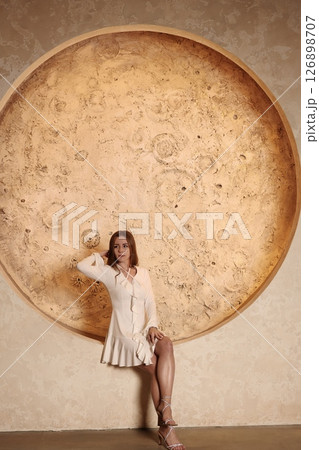 An Elegant Woman Posing Gracefully by a Beautiful Textured Circle Wall Art Piece 126898707