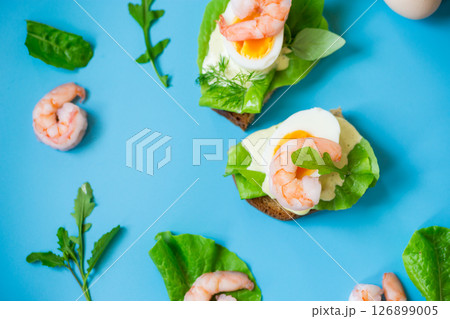 Appetizing breakfast with shrimp, egg and greens on top on blue background Appetizing breakfast with shrimp, egg and greens on top on blue background 126899005