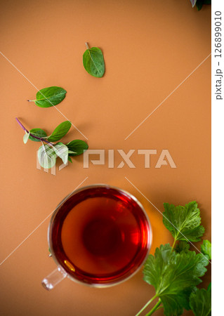 Green tea with currant leaves and mint in glass teapot and cup on brown background. Top view Green tea with currant leaves and mint in glass teapot and cup on brown background. Top view 126899010