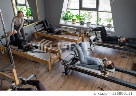 A group of woman exercises Glute bridge on a reformer bed machine in natural sunlight, focusing on pelvis and hips. 126899111