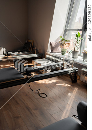 Modern Pilates studio with reformer beds bright, spacious windows for exercise and wellbeing Modern Pilates studio with reformer beds bright, spacious windows for exercise and wellbeing 126899120