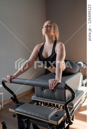 Woman training pilates on the reformer bed. Reformer pilates studio machine for fitness workouts in gym. Fit, healthy and strong authentical body. Fitness concept Woman training pilates on the reformer bed. Reformer pilates studio machine for fitness workouts in gym. Fit, healthy and strong authentical body. Fitness concept 126899123