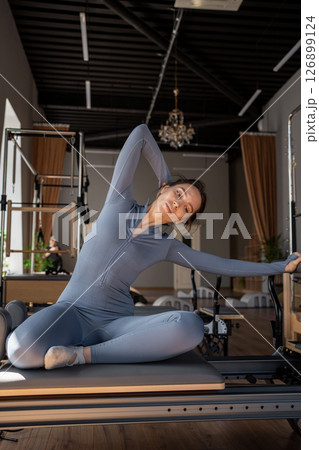 Woman doing mermaid exercise in a sunlite, modern pilates studio, embodying calm, focus, and strength. 126899124