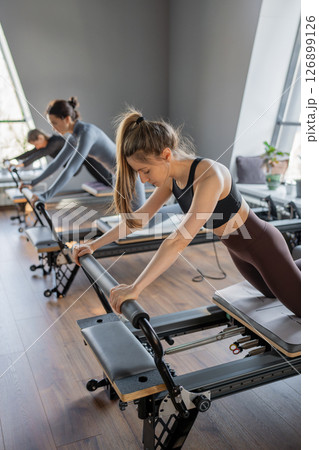 Woman training pilates on the reformer bed. Reformer pilates studio machine for fitness workouts in gym. Fit, healthy and strong authentical body. Fitness concept Woman training pilates on the reformer bed. Reformer pilates studio machine for fitness workouts in gym. Fit, healthy and strong authentical body. Fitness concept 126899126