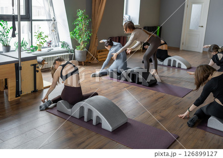 Woman doing mermaid exercise on back spine corrector. Reformer pilates studio machine for fitness workouts in gym. Fit, healthy and strong authentical body. Fitness concept. 126899127