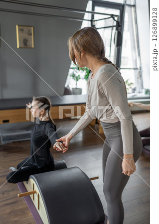 Woman doing mermaid exercise on back spine corrector. Reformer pilates studio machine for fitness workouts in gym. Fit, healthy and strong authentical body. Fitness concept. 126899128