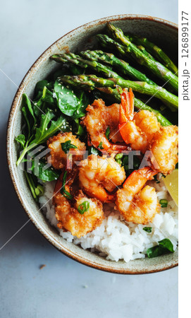 Breakfast features a bowl filled with crispy shrimp, vibrant asparagus, and spinach atop fluffy white rice, creating a balanced and enticing meal option 126899177