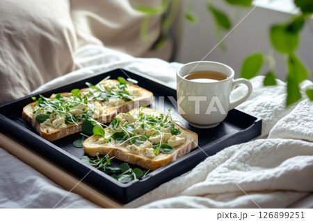 Freshly made creative toasts topped with various ingredients are presented on a wooden tray next to a steaming cup of tea, enhancing a relaxed morning atmosphere Freshly made creative toasts topped with various ingredients are presented on a wooden tray next to a steaming cup of tea, enhancing a relaxed morning atmosphere 126899251