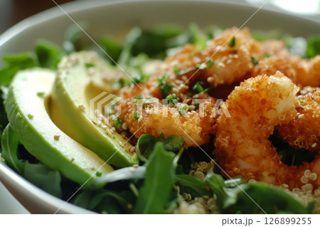 A vibrant breakfast bowl is presented with crispy shrimp, baby greens, and avocado slices, showcasing a delightful mix of textures and flavors perfect for the morning 126899255