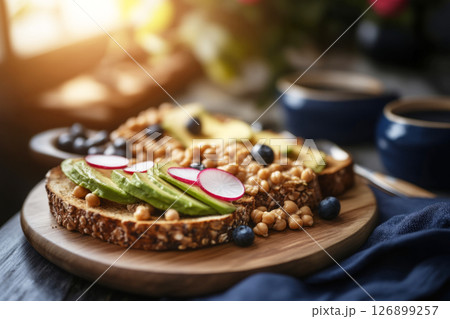 Bright morning light filters through a kitchen, highlighting a plate of artistic toast topped with avocado, radishes, sprouts, and chickpeas, perfect for a nourishing breakfast 126899257