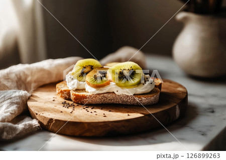 Breakfast is served with delightful toasts topped with creamy yogurt, fresh kiwi, and chia seeds on a rustic wooden plate in a warm kitchen atmosphere 126899263