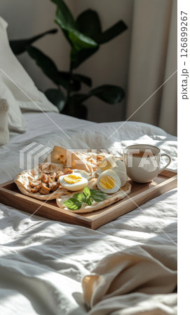 Savory pita with chicken, boiled egg, and yogurt dressing, along with a cup of hot tea, set on a white linen bed, creating a warm, cozy atmosphere with soft morning light 126899267