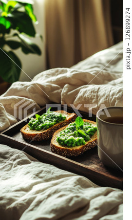 Freshly toasted bread topped with creamy avocado and herbs is served in bed with a cup of green tea, creating a perfect breakfast to enjoy on a leisurely morning Freshly toasted bread topped with creamy avocado and herbs is served in bed with a cup of green tea, creating a perfect breakfast to enjoy on a leisurely morning 126899274
