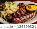 Savory bratwurst grilled to perfection alongside fresh sauerkraut and a side of mustard, served in a warm and inviting atmosphere ideal for a hearty meal 126899321