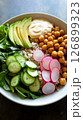 A vibrant breakfast bowl features chickpeas, sliced avocado, fresh cucumber, and radishes over grains, garnished with a dollop of sauce, perfect for a healthy start 126899323