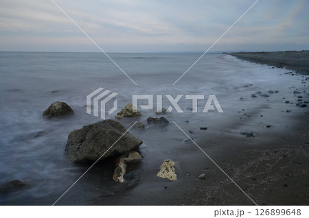 Gentle waves lap against rocky shoreline at dusk, creating a serene coastal atmosphere filled with tranquility and nature's beauty Gentle waves lap against rocky shoreline at dusk, creating a serene coastal atmosphere filled with tranquility and nature's beauty 126899648