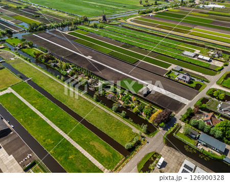 Aerial view of Dutch farmland with green fields, canals, and a traditional windmill. Neatly divided plots and vibrant vegetation highlight the beauty of rural agricultural landscape. Aerial view of Dutch farmland with green fields, canals, and a traditional windmill. Neatly divided plots and vibrant vegetation highlight the beauty of rural agricultural landscape. 126900328