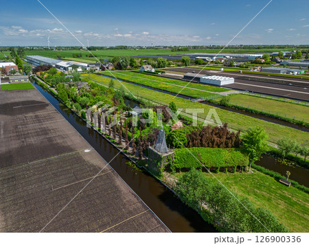 Aerial view of a lush countryside garden surrounded by canals and farmlands, with a cozy house and colorful trees, set in a peaceful rural landscape under a clear blue sky. Aerial view of a lush countryside garden surrounded by canals and farmlands, with a cozy house and colorful trees, set in a peaceful rural landscape under a clear blue sky. 126900336