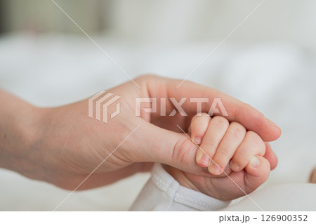 Happy family. Tiny newborn infant baby little hand on mother hand palm. Newborn baby holding parent finger after birth. Mom baby at home. Support protection of new life. Handle with care 126900352