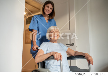 Young female nurse carrying a wheelchair with an elderly woman 126901158