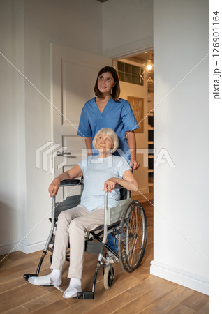 Young female nurse carrying a wheelchair with an elderly woman 126901164