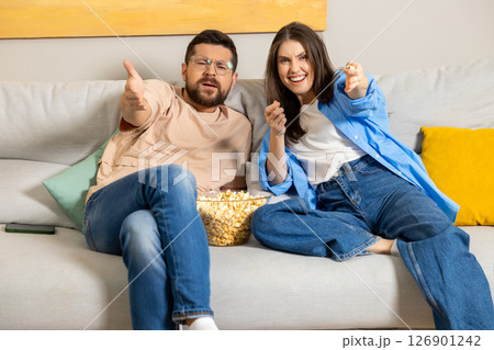 Couple enjoying cozy evening at home watching movie together with popcorn on sofa 126901242