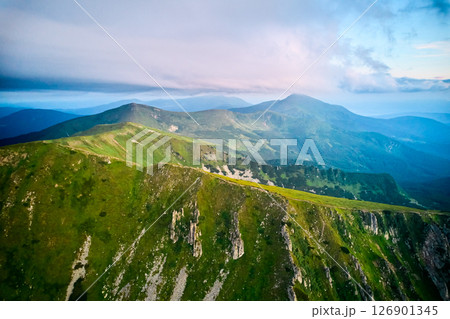 Breathtaking aerial view of green, rugged mountain peaks under dramatic sky. Scene captures contrast between vibrant landscape and moody clouds, with sunlight breaking through. Carpathians, Chornogora 126901345