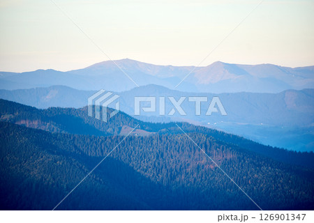 Serene view of rolling mountains in shades of blue and green, with distant peaks under soft, pastel sky, creating peaceful and tranquil landscape. 126901347