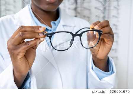 African american optometrist in a lab coat holding new eyeglasses in hands 126901679